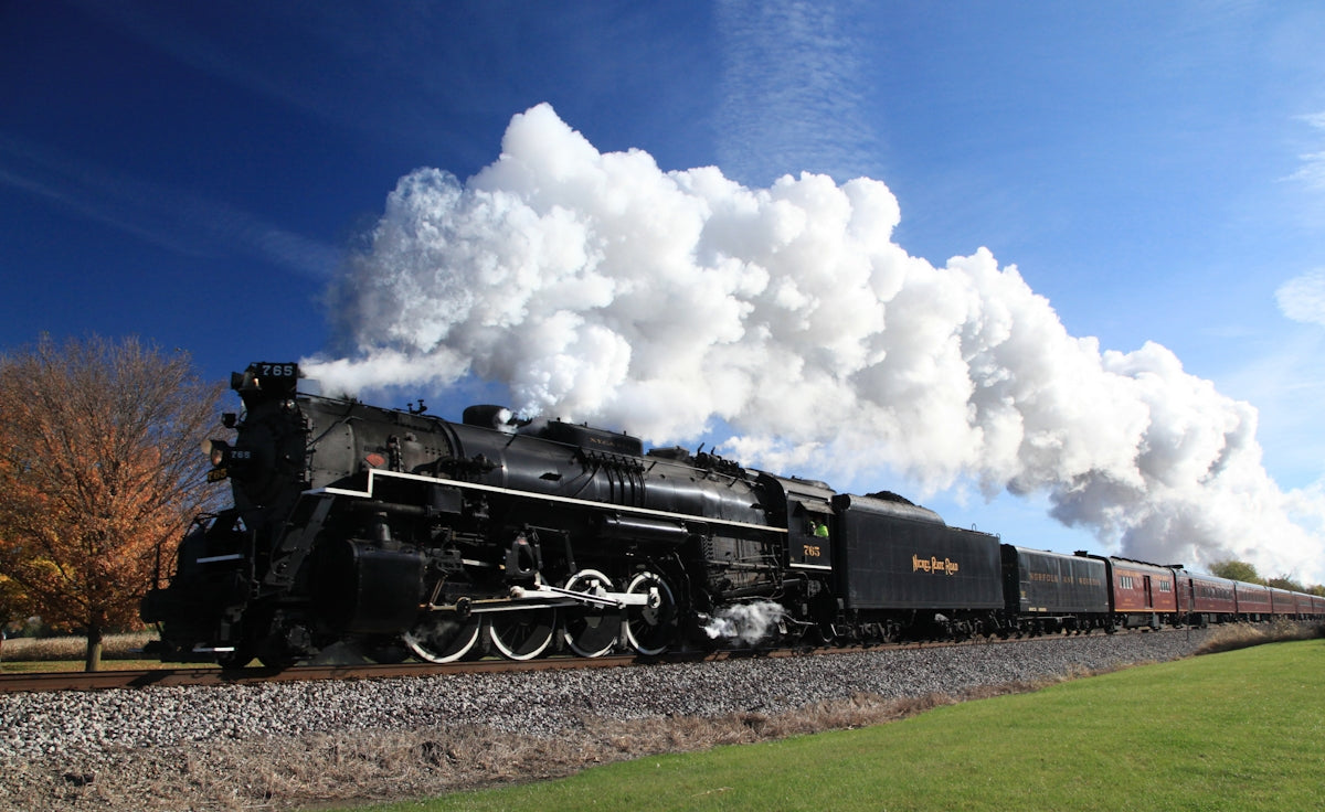 a black train traveling down train tracks next to a lush green field