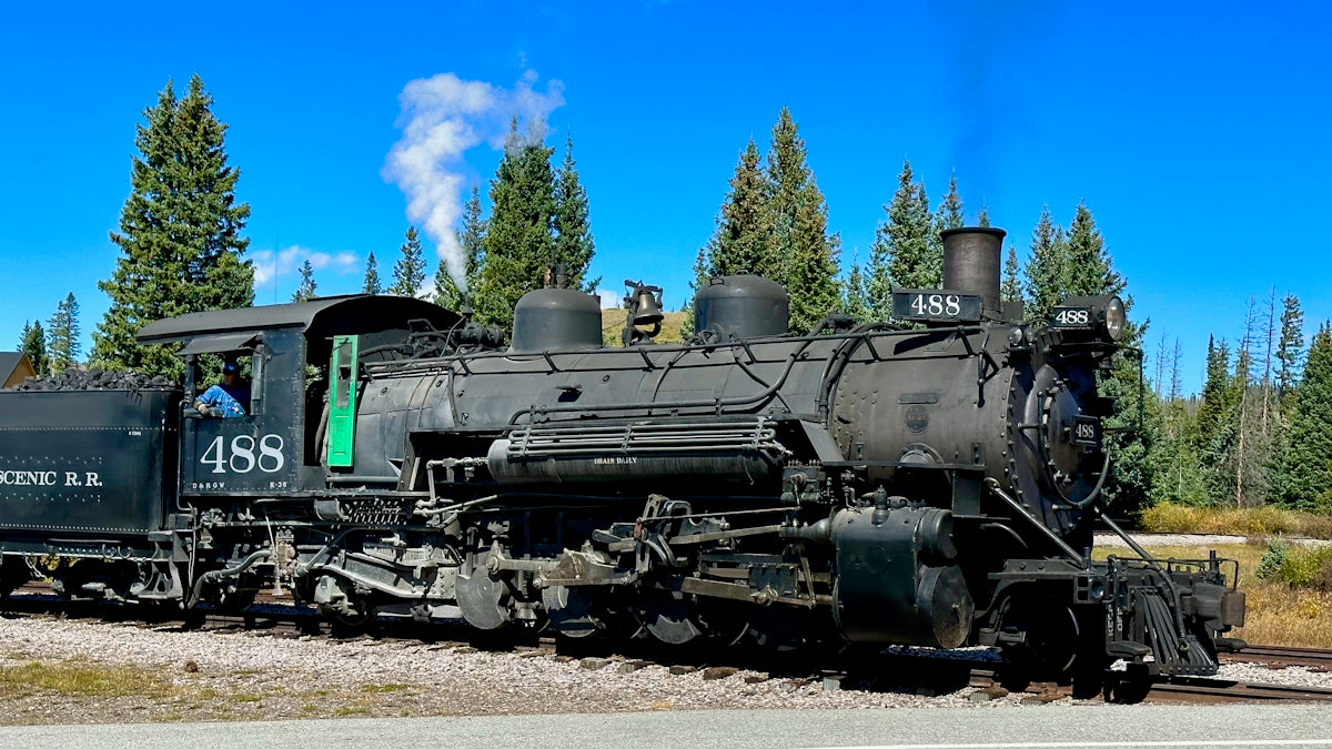 a black train traveling down train tracks next to a forest